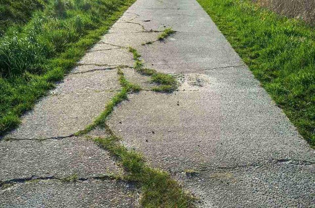 Cracked and damaged concrete driveway with visible wear and weeds growing through the surface in Parma Heights, OH